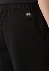 Černé kalhoty vyrobené z hladkého materiálu s elastickým pasem. Na zadní kapse je malá značka.