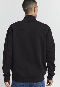 Sort sweatshirt med høj krave, afslappet pasform og ribbede manchetter og kant. Glat tekstur, minimal detaljer og ingen synlige logoer.