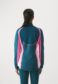 Teal Sportjacke mit pinken und weißen Akzenten; verfügt über einen hohen Kragen, lange Ärmel und ein figurbetontes Design, hergestellt aus atmungsaktivem Material.