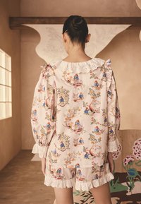 Strój w kwiatowy wzór z jasnoróżowej tkaniny, z falbankowym kołnierzem i koronkowym wykończeniem na rękawach i szortach. Widoczne dekoracyjne ilustracje.