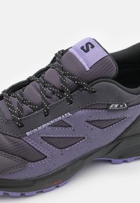 Fioletowe i czarne buty trekkingowe charakteryzują się trwałą tekstylną cholewką, teksturowanymi nakładkami, etykietą wodoodporną oraz wielopodłogową podeszwą.