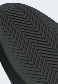 Čierna podrážka topánky s cikcakovým vzorom dezénu, textúrovaným povrchom a zosilnenými okrajmi pre odolnosť a priľnavosť.