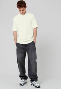 T-shirt blanche à manches courtes avec une coupe décontractée, associée à un jean gris ample. Porté avec des baskets grises et noires. Design simple.