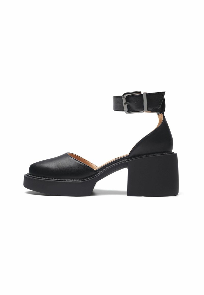 Sandale en cuir noir avec un bout arrondi, une bride de cheville et un talon épais. Présente une texture lisse et des détails de couture minimal.