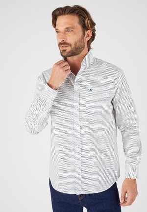 Camicia bianca con bottoni, caratterizzata da un motivo geometrico blu navy, maniche lunghe e colletto a punta. Il tessuto è liscio e presenta una leggera lucentezza.