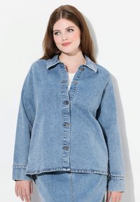 Chaqueta de mezclilla de color azul claro con un corte holgado, cierre de botones y cuello clásico. Presenta un dobladillo ligeramente deshilachado y dos bolsillos frontales.