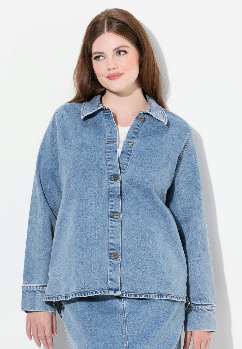 Chaqueta de mezclilla de color azul claro con un corte holgado, cierre de botones y cuello clásico. Presenta un dobladillo ligeramente deshilachado y dos bolsillos frontales.