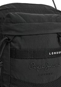 Zaino nero con un'esterno in nylon texture, tasca frontale con cinturino e logo "Pepe Jeans London" impresso. Chiusura con cordoncino regolabile.