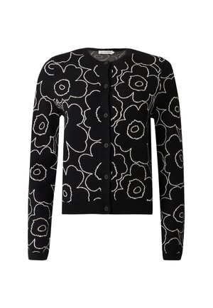 Femme portant un cardigan noir avec des contours floraux blancs, une jupe bicolore noire et rose, et des sandales noires à talons ouverts.
