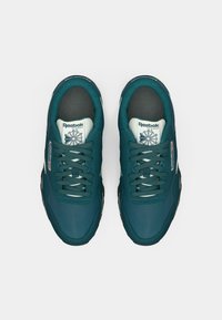 Par čizama Reebok Classic u tirkiznoj boji s bijelim oznakama na jeziku i tamnim potplatima, prikazanima odozgo na bijeloj pozadini.