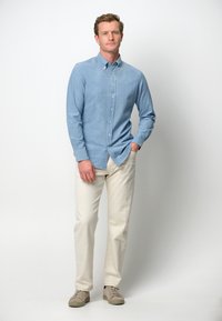 Camicia button-up azzurro chiaro con maniche lunghe, abbinata a pantaloni beige e sneakers chiare. Design semplice e look casual.