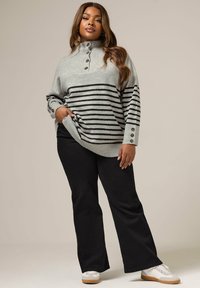 Pull gris rayé avec un col haut et des accents de boutons sur les manches. Associé à un pantalon noir évasé et des baskets blanches.