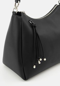 Schwarze Lederhandtasche mit glatter Textur, klarer Form, silberner Hardware und dekorativen Quasten mit Perlenakzenten.