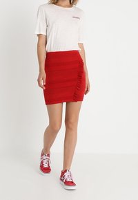 Červená minisukně s texturou a volánkovým detailem na boku, kombinovaná se světle béžovou košilí a červenými teniskami.