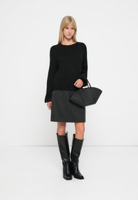 Suéter preto de malha, saia lápis cinza e botas de couro pretas até ao joelho. A modelo segura uma bolsa estruturada preta. Design minimalista, cores sólidas.