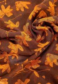 Tessuto marrone con una consistenza morbida, caratterizzato da un motivo che presenta foglie e steli arancioni su tutta la superficie. Il design è organico e ha un aspetto fluido.