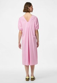 Roza karirana haljina sa kratkim izbočenim rukavima, V-izrezom na leđima i dužinom do sredine teladi. Ima središnji nabor na leđima za dodatnu pokretljivost. Udoban dizajn.