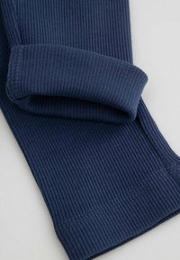 Granatowe legginsy o prążkowanej strukturze, wykonane z miękkiego materiału, z wywijanym mankietem. Tkanina ma pionowe żłobienia i estetyczne wykończenie dołów.