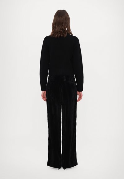 Schwarzer, kurz geschnittener Pullover mit geripptem Saum, kombiniert mit schwarzen, weit geschnittenen, plissierten Hose. Glatte Textur, keine sichtbaren Muster oder Hardware-Details.