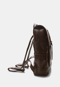 Zaino in pelle marrone con forma strutturata, dotato di apertura con zip, spallacci regolabili e tasca frontale. Superficie testurizzata e dettagli di cucitura.