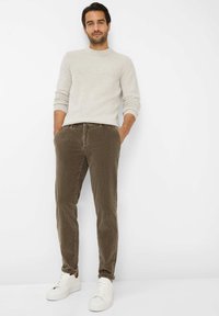 Maglione grigio chiaro lavorato a maglia con texture a coste, abbinato a pantaloni in velluto a coste verde oliva e sneakers bianche. Il modello è in piedi con le mani nelle tasche.