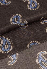 Mørkebrunt stof med et paisley-mønster i blå og creme, med fine frynser langs kanterne. Blød, let tekstur.
