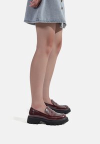 Mocassini bordeaux lucidi con una suola nera spessa e un design a tasca per il penny. Abbinati a una gonna di jeans, che mettono in risalto uno stile casual.