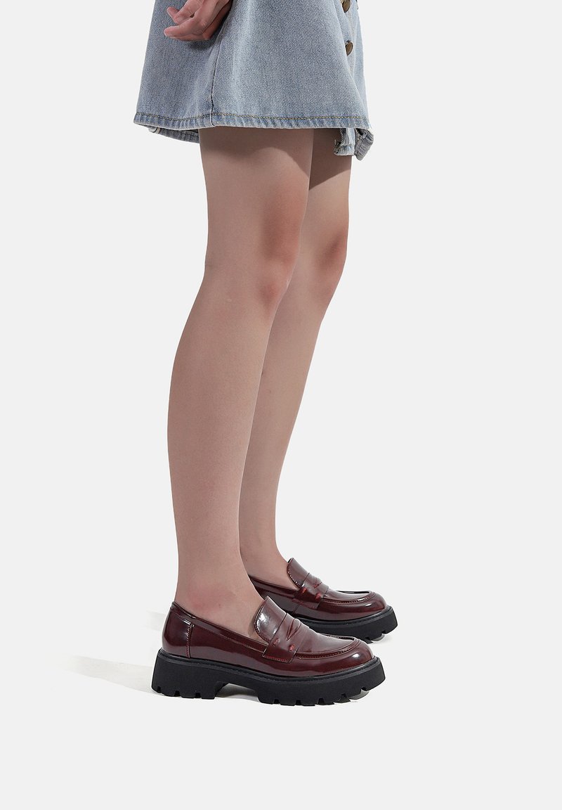 Mocassini bordeaux lucidi con una suola nera spessa e un design a tasca per il penny. Abbinati a una gonna di jeans, che mettono in risalto uno stile casual.