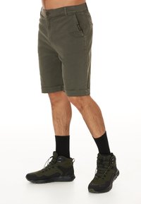 Olivgröna shorts med knappstängning och uppvikta fållar, med sidfickor. I kombination med svarta halvhöga vandringsskor och mörka strumpor.
