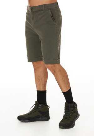 Olivgröna shorts med knappstängning och uppvikta fållar, med sidfickor. I kombination med svarta halvhöga vandringsskor och mörka strumpor.