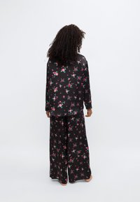 Ensemble de pyjama noir à motifs floraux comprenant un haut à manches longues et un pantalon à jambes larges avec un motif floral vibrant en rouge et vert. Tissu doux au toucher.