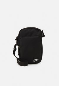 Borsa a spalla nera Nike di piccole dimensioni con tasca frontale con zip, tracolla regolabile e logo Nike bianco nell'angolo in basso a destra.