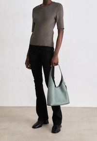 Top corto a righe marrone, pantaloni neri attillati e una borsa in pelle verde menta con un design curvo. Stivaletti neri completano l'outfit.