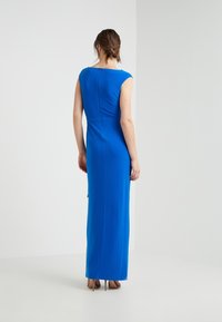 Blue, sleeveless maxi dress with a fitted silhouette, smooth texture, and a small back zipper detail. Floor-length design.