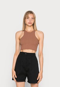 Top cropped canelado castanho com decote alto, combinado com calções pretos de cintura alta, apresentando um botão e pormenor de pregas.