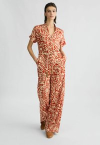 Rode en crèmekleurige jumpsuit met een patroon, korte mouwen, kraag, trekkoord in de taille en zijzakken; gemaakt van lichtgewicht stof.