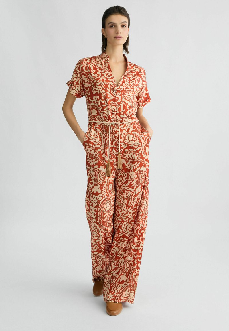 Rode en crèmekleurige jumpsuit met een patroon, korte mouwen, kraag, trekkoord in de taille en zijzakken; gemaakt van lichtgewicht stof.