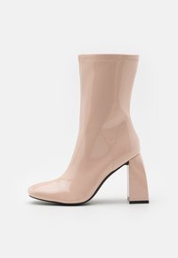 Ankelstøvle i lys pink laklæder med spids tå og en chunky, transparent blokhæl. Sømdetaljer er synlige langs siderne.