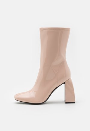 Bottines en cuir verni de couleur rose pâle, avec un bout pointu et un large talon bloc transparent. Des coutures sont visibles le long des côtés.
