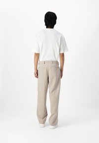 T-shirt bianca a maniche corte e pantaloni beige dal taglio morbido con cinturino piatto e tasche posteriori, abbinati a sneakers bianche.