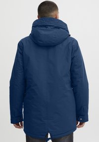 Tumši zilas krāsas, polsterēta parka ar lielu kapuci. Aprīkota ar auklu apakšmalā un spiedpogu aizdares pie piedurknēm. Gluda, ūdensizturīga virsma.