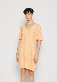 Robe à manches courtes de couleur orange clair avec un imprimé floral, décolleté en V et coupe décontractée. Fabriquée dans un tissu doux avec un léger éclat.