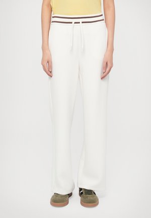 Pantalon de survêtement blanc à jambes larges, doté d'une ceinture élastique rayée marron avec un cordon de serrage. Le tissu semble doux avec une texture lisse.