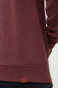 Maroon sweatshirt featuring a soft texture, ribbed hem, and a small leather logo tag near the bottom. Long sleeve with a relaxed fit.