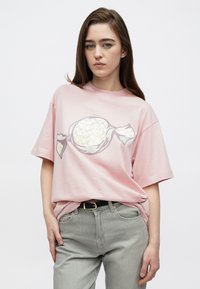 Ροζ υπερμεγέθη μπλουζάκι με γραφικό καραμελάκι σε λευκό και ασημί, φορεμένο με ανοιχτό γκρι τζιν, που παρουσιάζει άνετη εφαρμογή και μαλακή υφή.