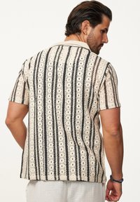 Beige Kurzarmhemd mit schwarzen und weißen vertikalen Streifen. Verfügt über ein strukturiertes Muster und eine lockere Passform, die sich gut für legere Anlässe eignet.