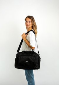 Fekete sporttáska, tartós anyagból készült, kettős markolattal, levehető vállpánttal és elülső cipzáras zsebbel a könnyű hozzáférés érdekében.