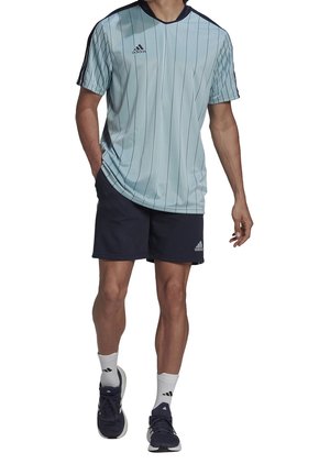 Ljusblå atletisk tröja med vertikala ränder, korta ärmar och mörkblå detaljer; tillsammans med marinblå shorts och svarta träningsskor.