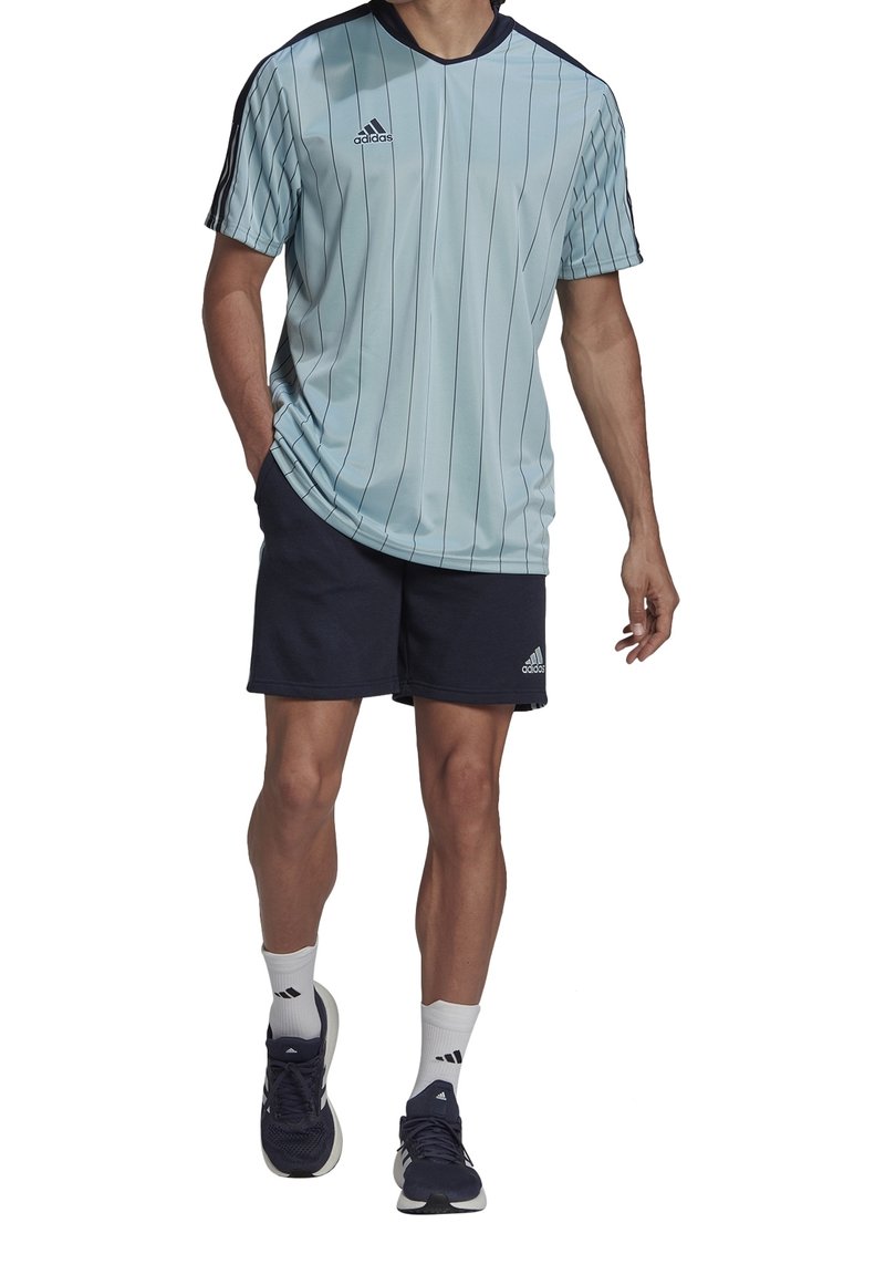 Maillot de sport bleu clair avec des rayures verticales, manches courtes et accents bleu foncé ; associé à un short marine et des chaussures de sport noires.