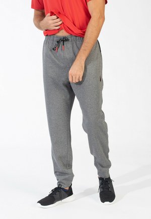 Graue gestrickte Sweatpants mit einem elastischen Taillenbund, Zugbandakzenten, schmal zulaufenden Beinen und Seitentaschen, kombiniert mit schwarzen Sneakers.